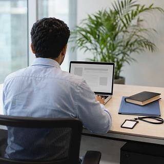 A learner at a tidy office desk seen from behind, working through an application on a laptop